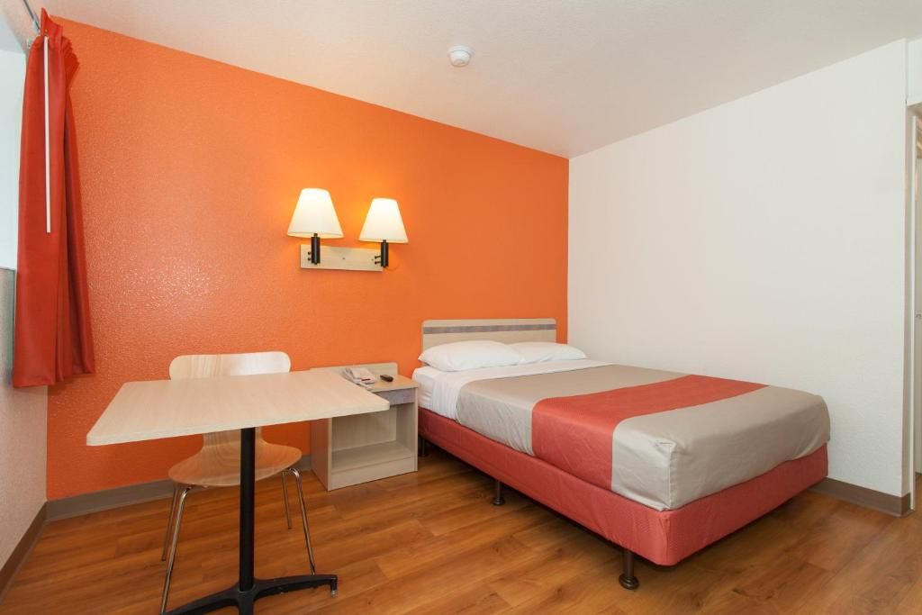 A hotel room with a bed, a desk, and a chair. There are two wall-mounted lamps.