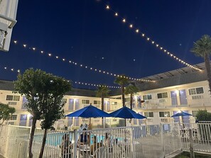 A hotel courtyard with a swimming pool, outdoor seating, and string lights. - Hi-Wheel Flats (Davis)