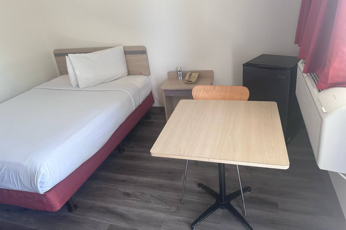A small hotel room with a single bed, a wooden table, a small desk with a telephone, and a radiator.