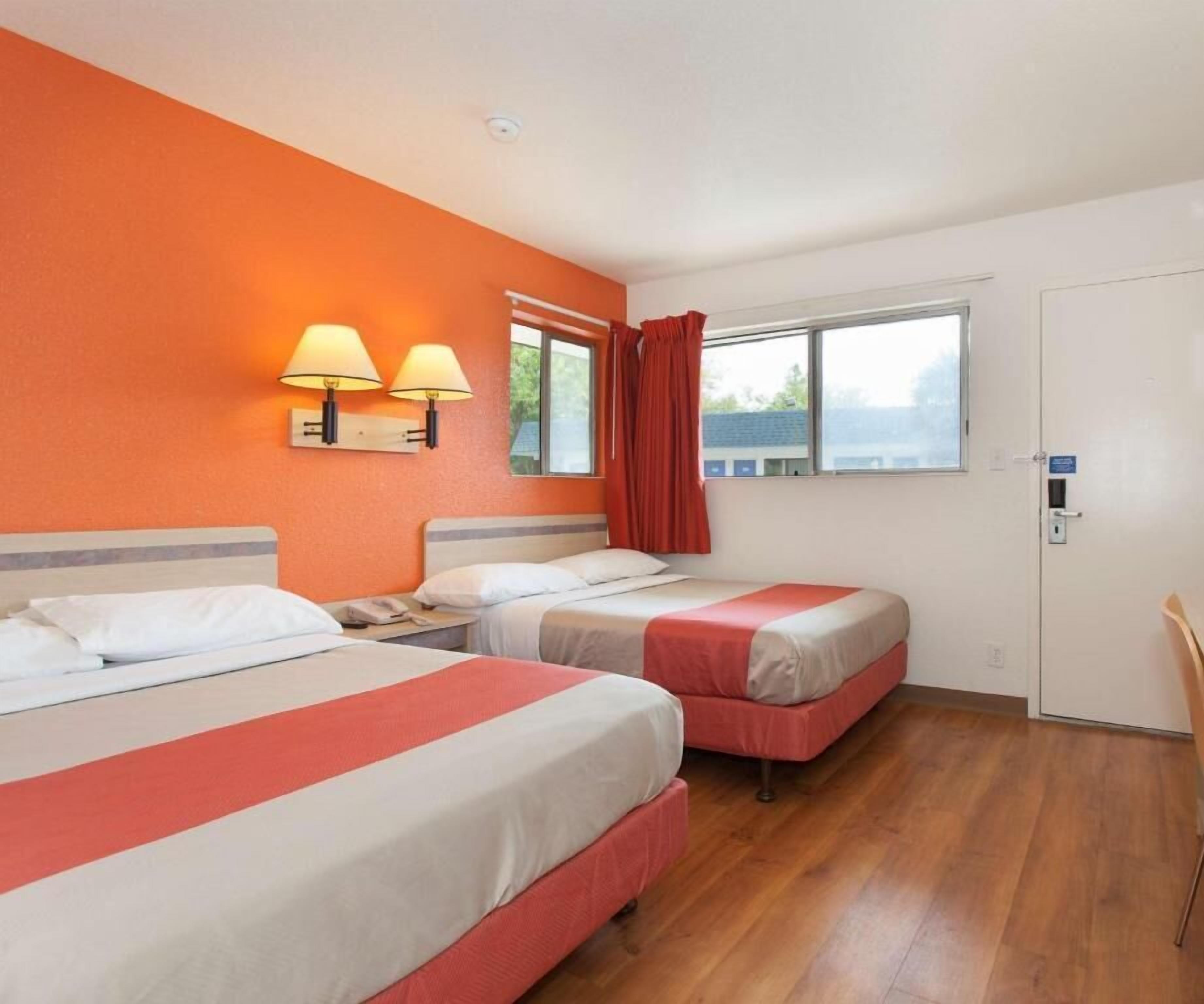 A hotel room with two beds, a window with curtains, and a nightstand with a lamp.