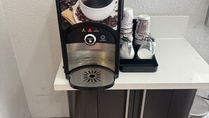 Eine Kaffeemaschine mit einer Kaffeetasse, einem Milchaufschäumer und einem Zuckerbehälter auf einer Arbeitsplatte.