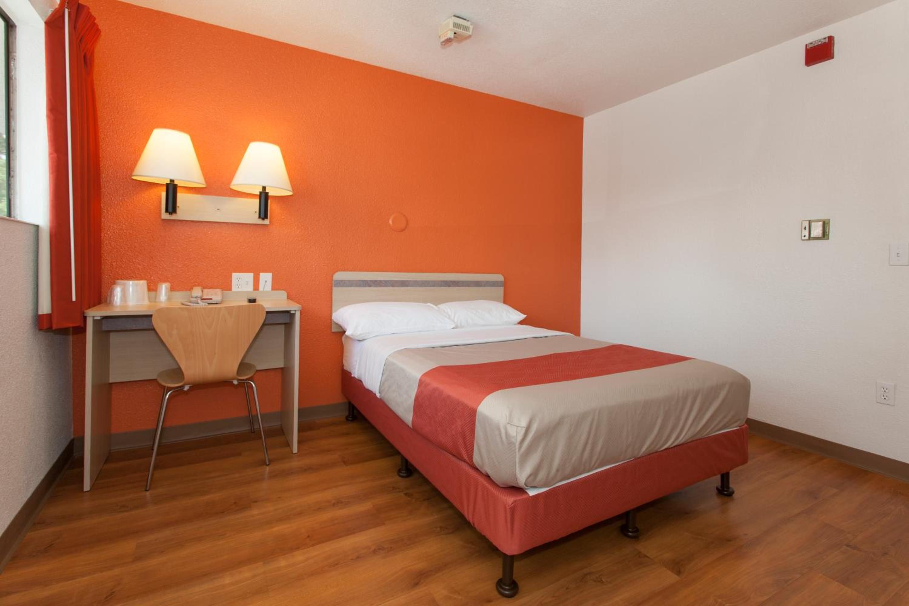 A hotel room with a bed, a desk, and two wall-mounted lamps.