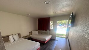Ein Hotelzimmer mit zwei Betten, einem Holztisch, einem Fernseher und einem Fenster mit Blick nach draußen.