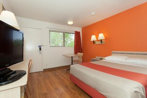 Una habitación de hotel con cama, escritorio, televisor y dos lámparas de pared.