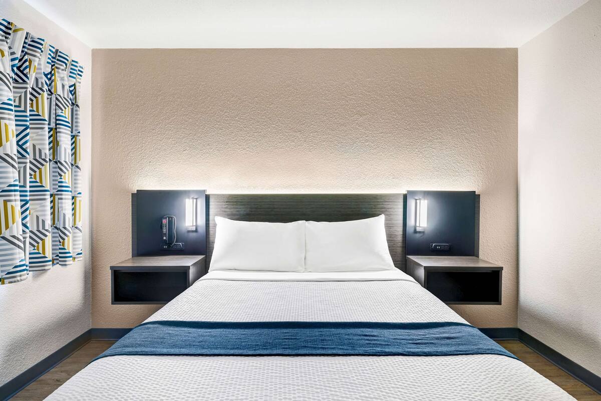 A hotel room with a large bed, two bedside tables, a headboard, and a wall-mounted light fixture.
