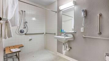 Een badkamer met douche, handgrepen, wastafel en spiegel.
