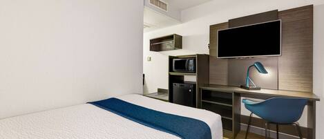 Une chambre d’hôtel moderne équipée d’un lit, d’un bureau, d’une chaise, d’une télévision et d’un four à micro-ondes.