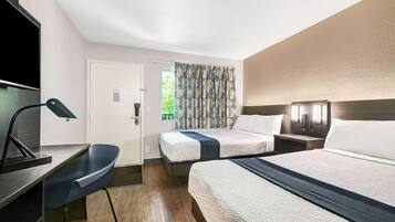 Une chambre d’hôtel équipée d’un lit, d’un bureau, d’une chaise, d’une télévision et d’une fenêtre avec des rideaux à motifs.