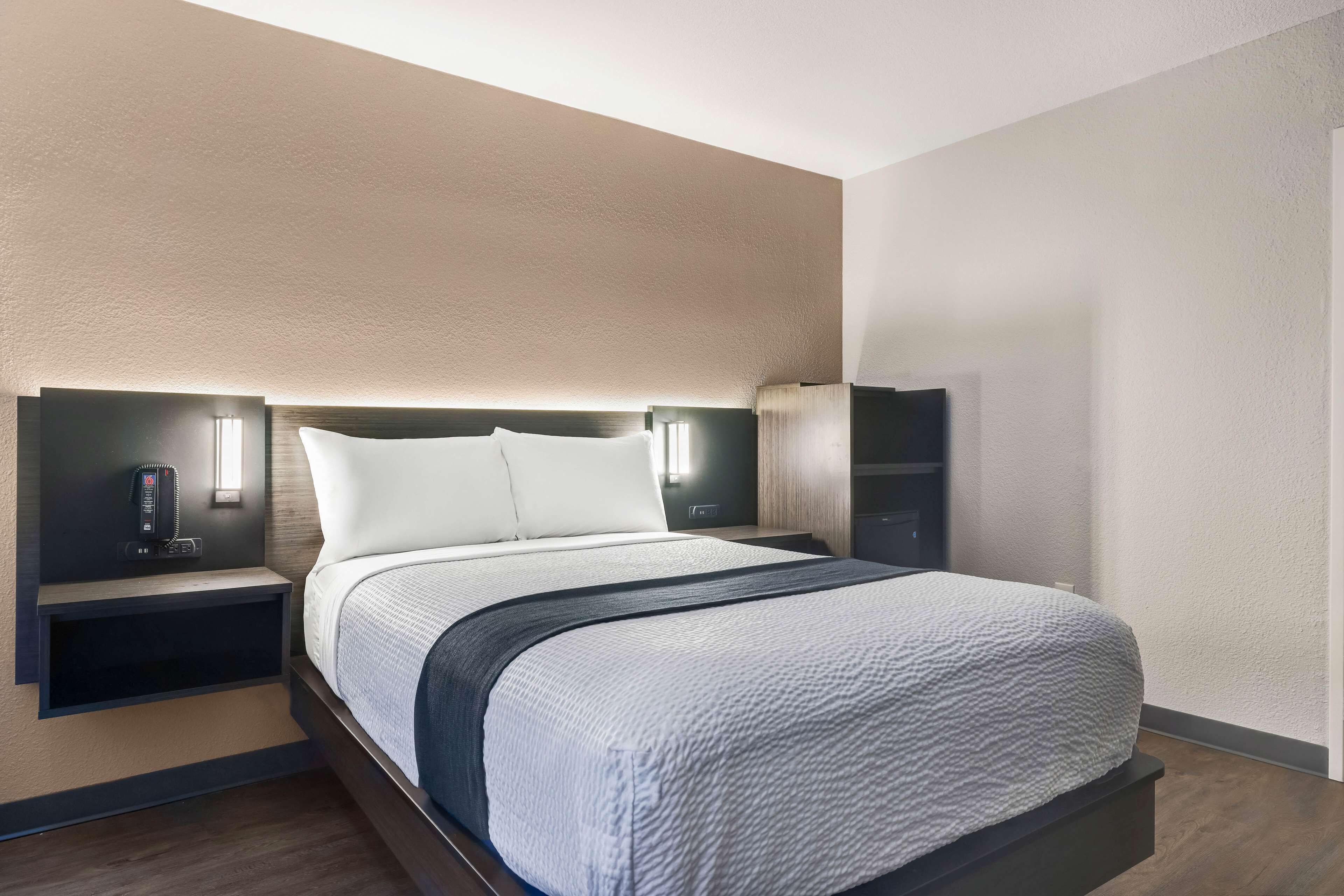 A modern hotel room with a large bed, bedside tables, and wall-mounted lighting.