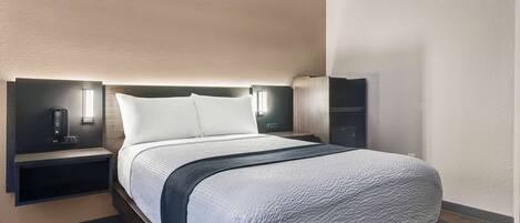 A modern hotel room with a large bed, bedside tables, and wall-mounted lighting.