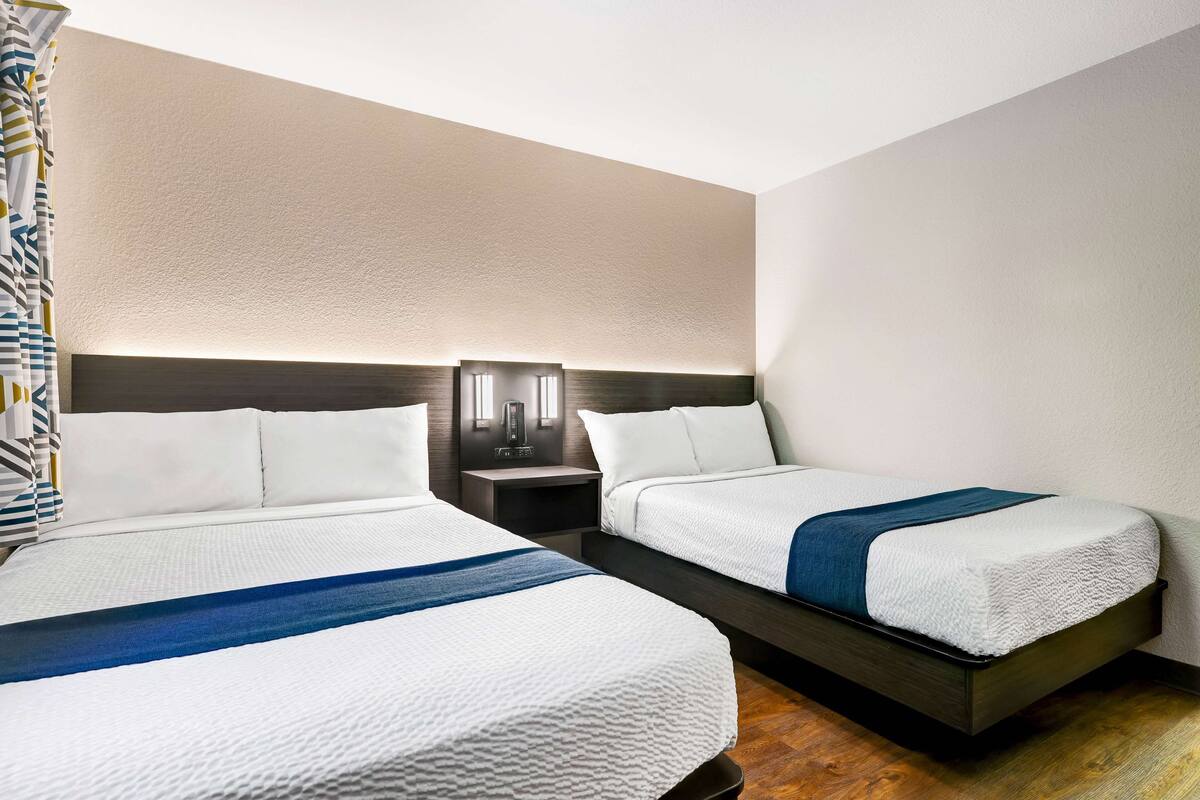 A hotel room with two beds, a nightstand, and a wall-mounted light fixture.