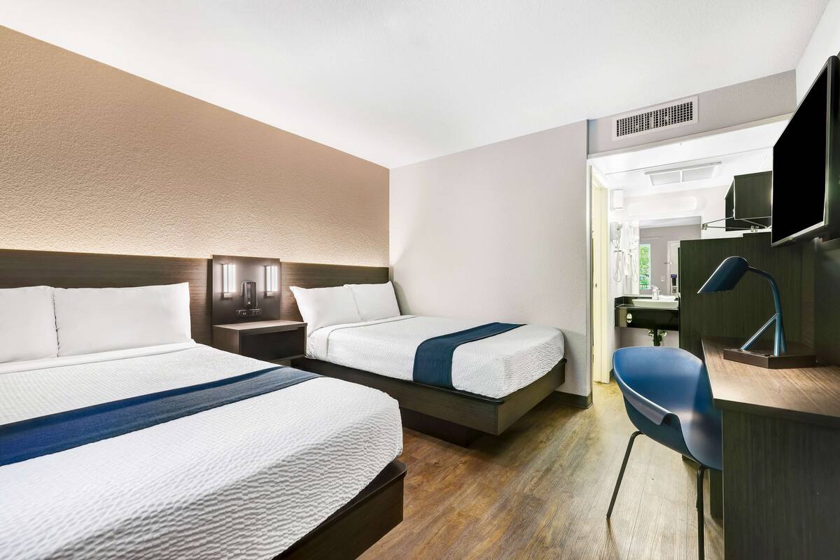 A hotel room with two beds, a desk, a chair, and a TV.