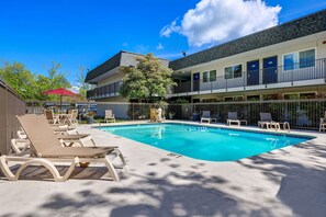 A swimming pool with lounge chairs, a red umbrella, and a building with balconies.