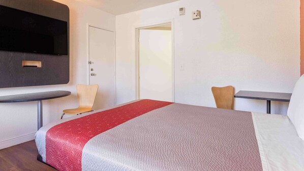 A hotel room with a bed, a small table, two chairs, a TV mounted on the wall, and a door.
