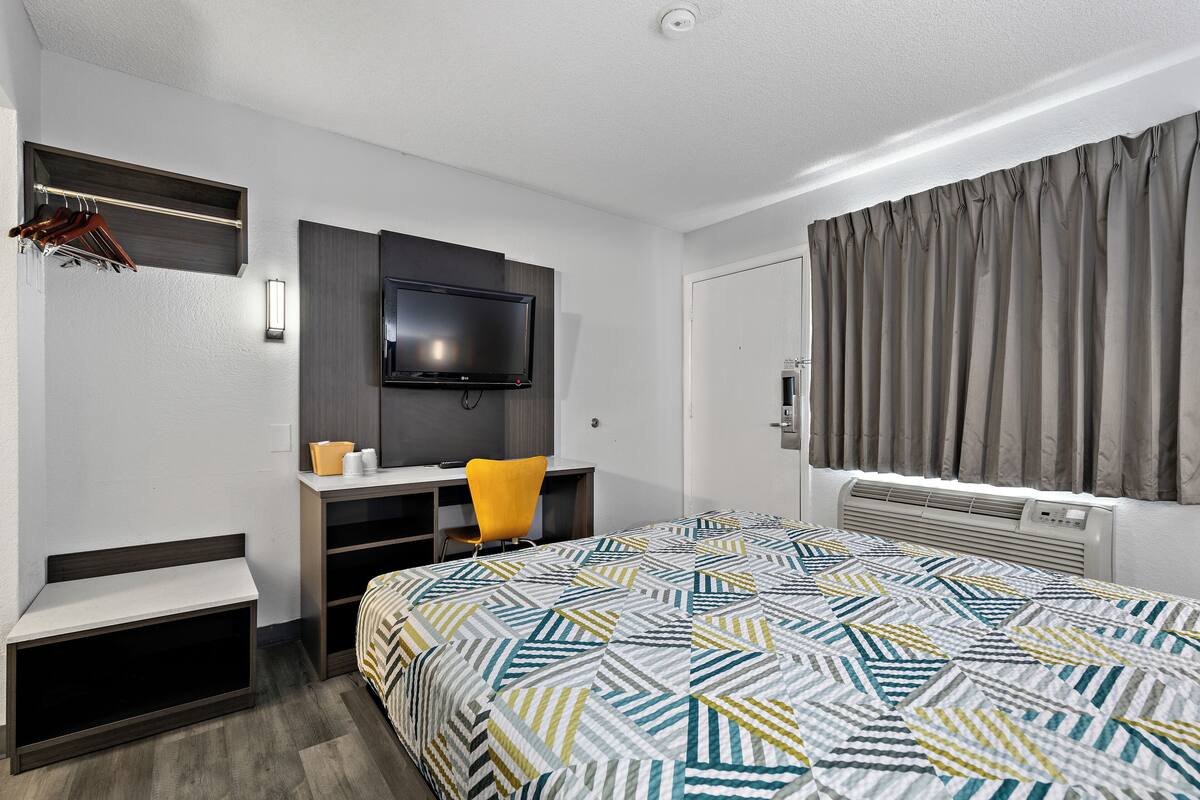 A hotel room with a bed, a desk, a chair, a television, and a window with curtains.