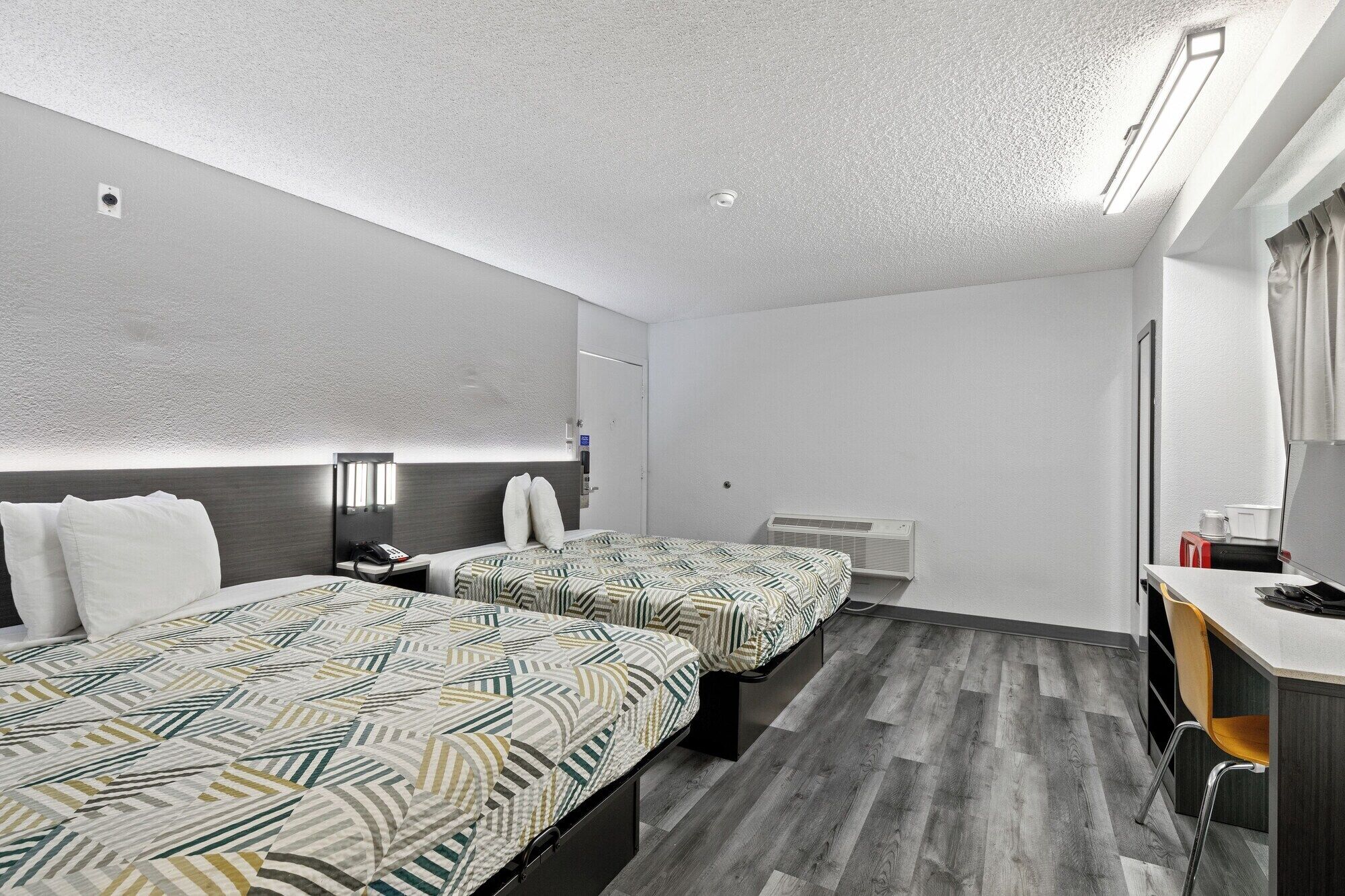Habitación de hotel con dos camas, un escritorio, una silla, un espejo y una ventana.