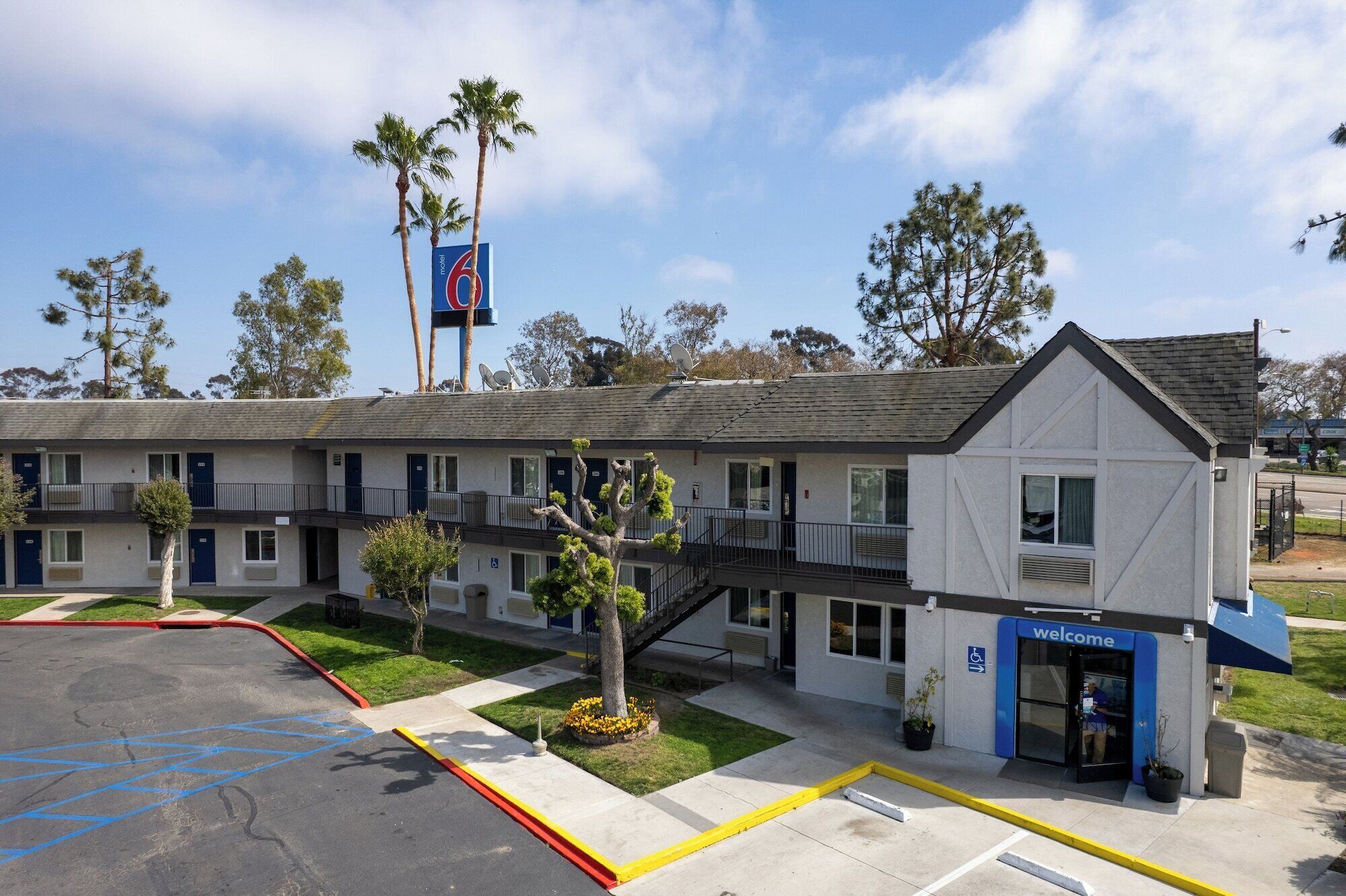 A motel with a 'Welcome' entrance, a parking lot with marked handicapped spaces, and a satellite dish on the roof.