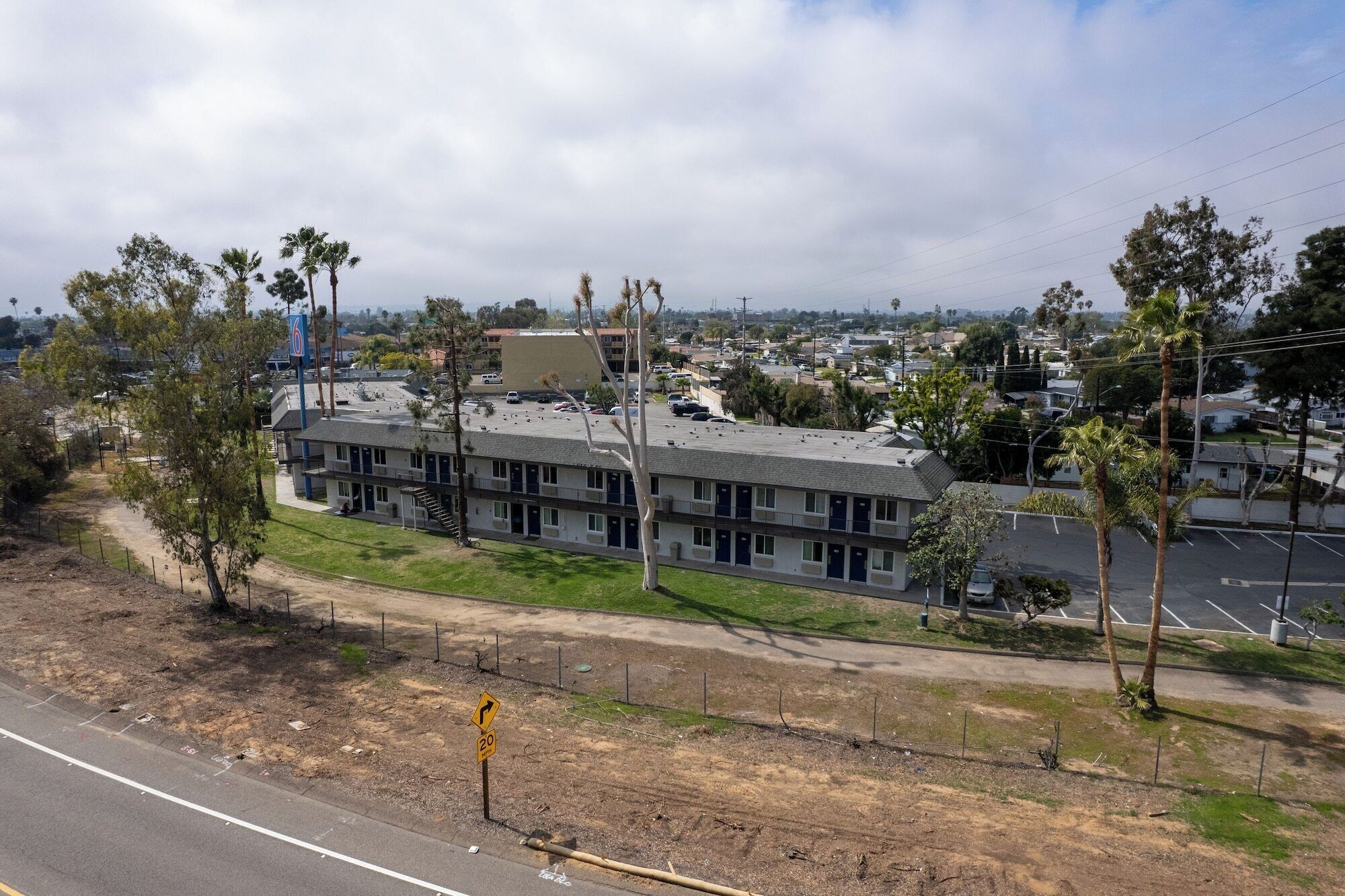 Un motel avec une rangée de chambres, un parking et un espace verdoyant avec des arbres.