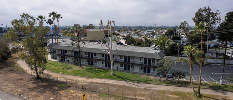 Un motel avec une rangée de chambres, un parking et un espace verdoyant avec des arbres.