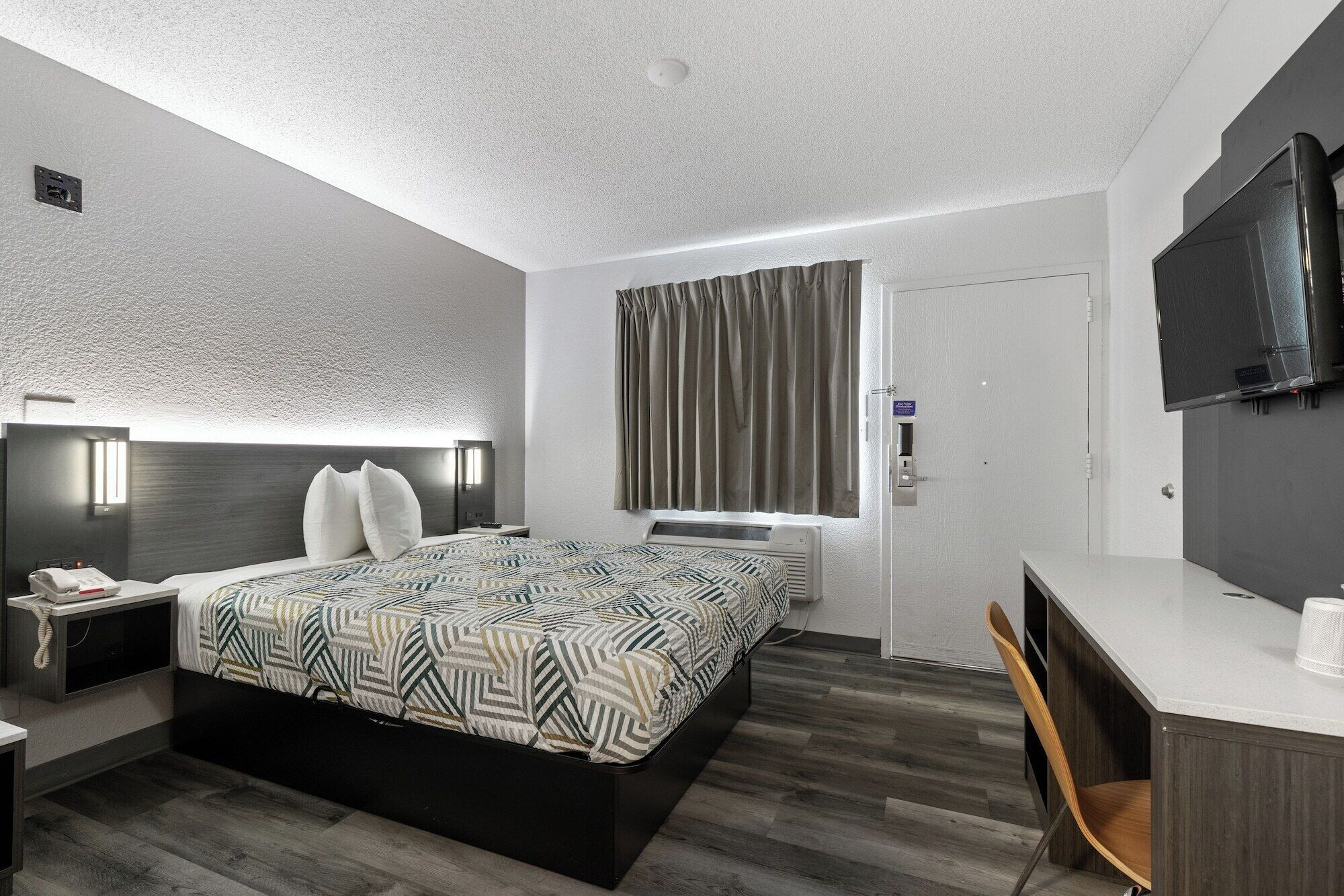 Una habitación de hotel moderna con una cama grande, una mesita de noche y un escritorio con una silla.