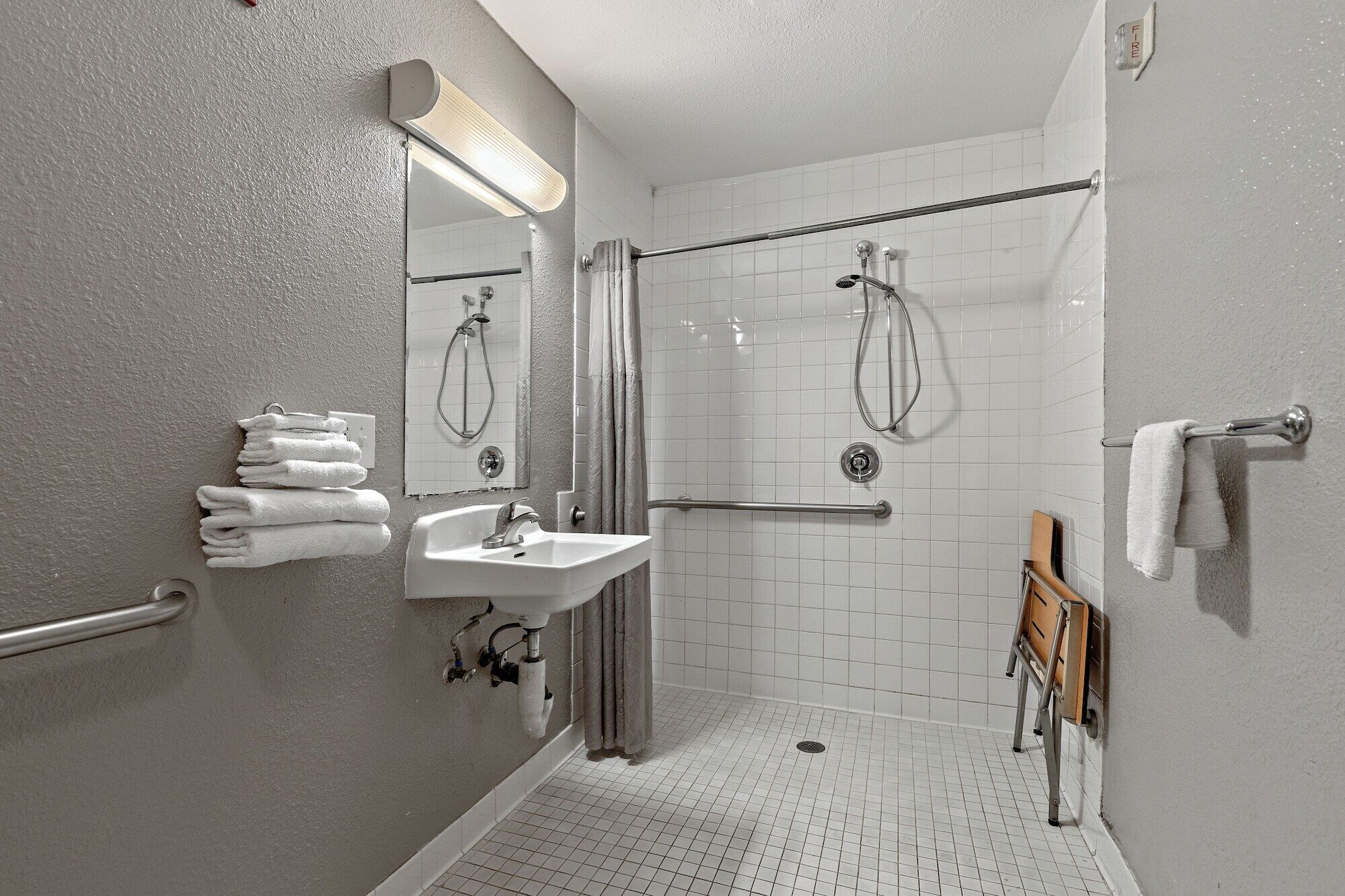 Een kleine badkamer met witte tegels, een wastafel, spiegel en douche.