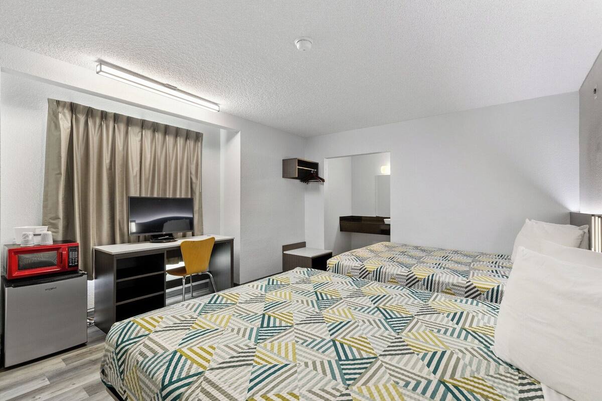 A hotel room with a bed, a desk with a computer, a microwave, and a small refrigerator.