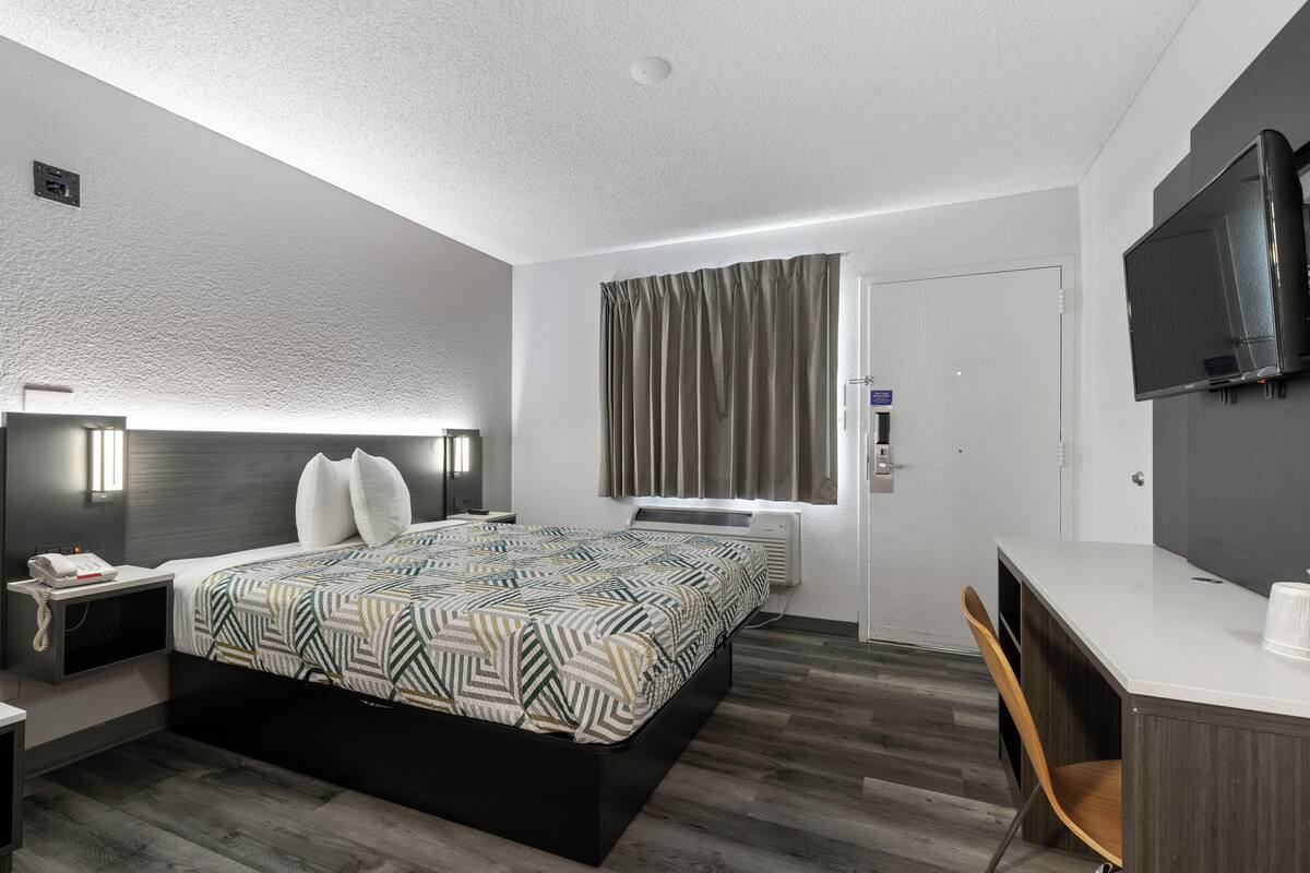 A modern hotel room with a large bed, a desk, a chair, a flat-screen TV, and a window with curtains.