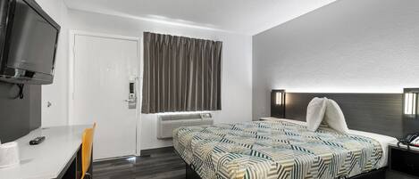 Una habitación de hotel moderna con cama, escritorio, silla, televisor y ventana con cortinas.