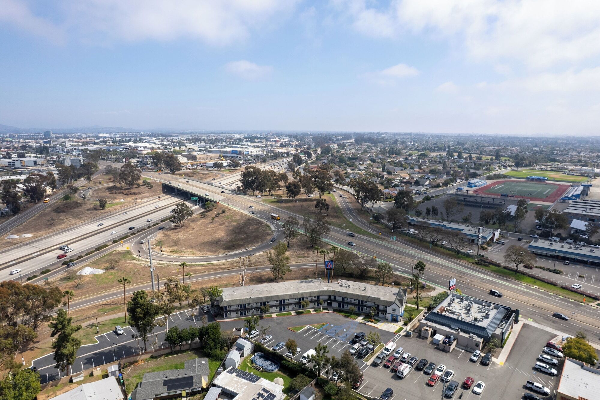 A multi-level parking structure with several levels of parking, a large building with a flat roof, and a highway interchange in the background.