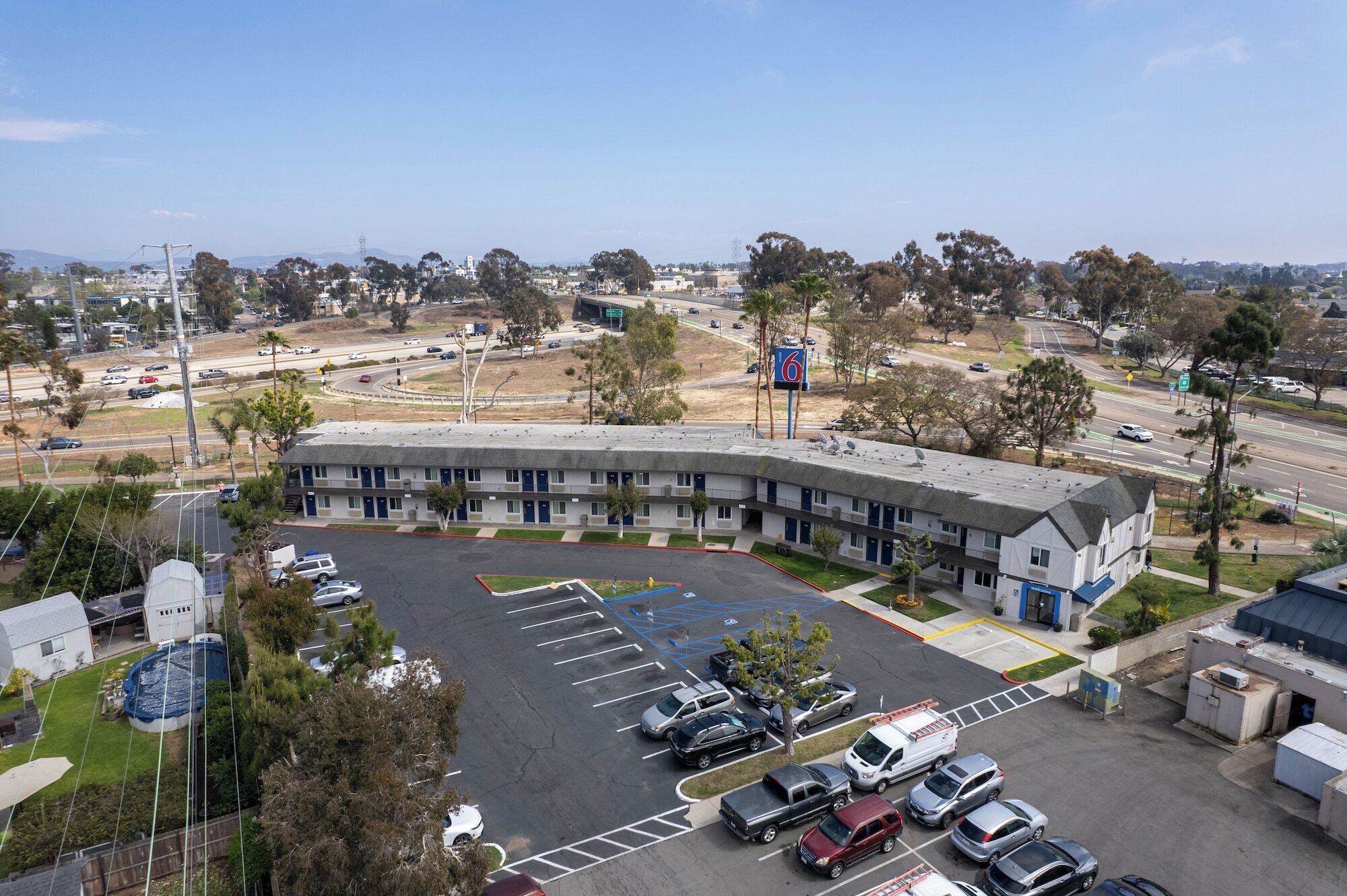 A motel with a parking lot, a swimming pool, and a view of the surrounding area.