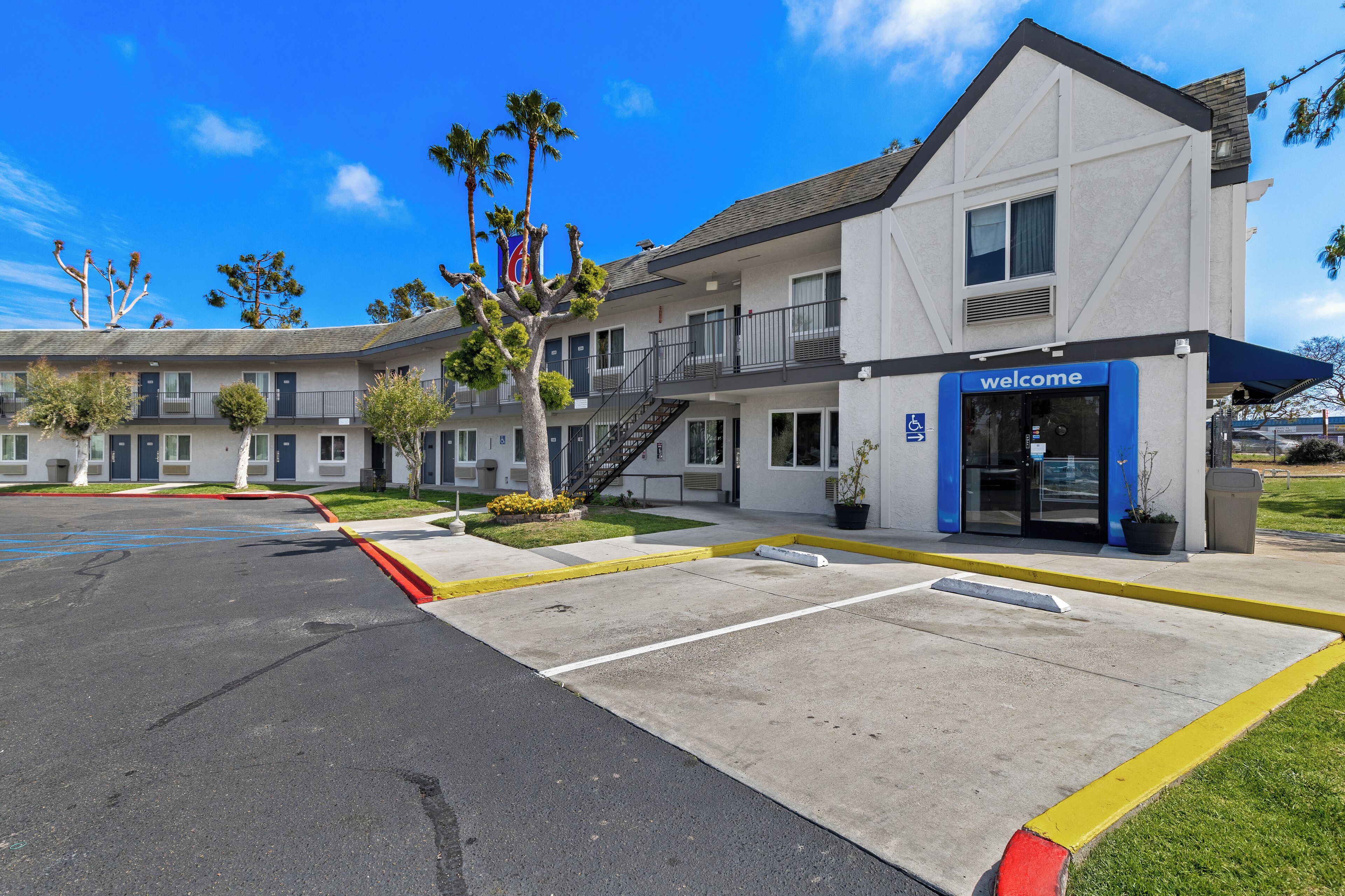 A motel with a 'welcome' sign, a parking lot, and a building with multiple floors and balconies.