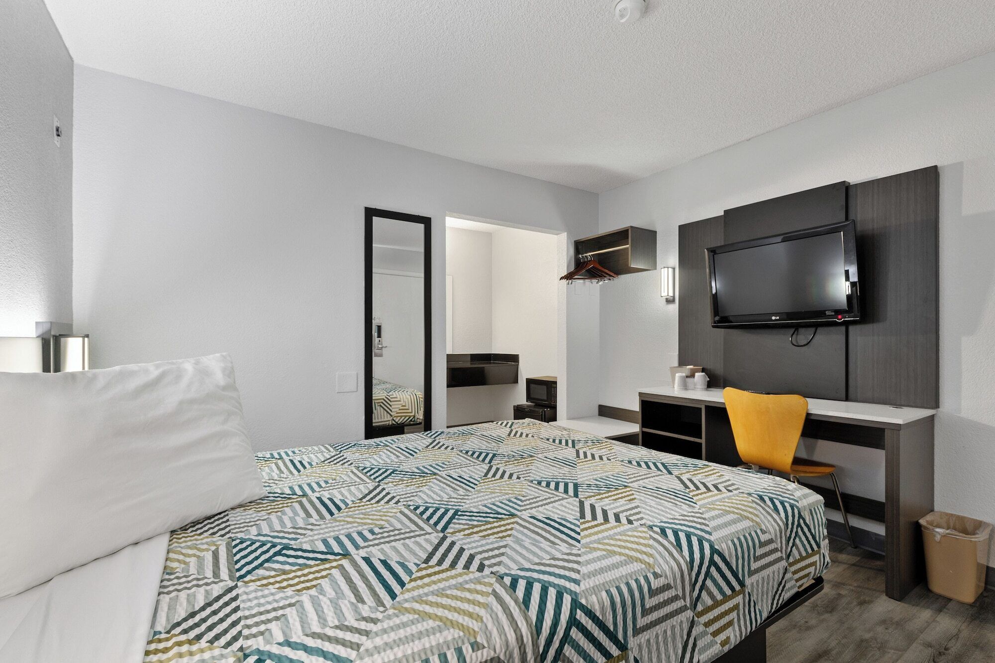 A hotel room with a bed, a desk with a chair, a television, and a mirror.