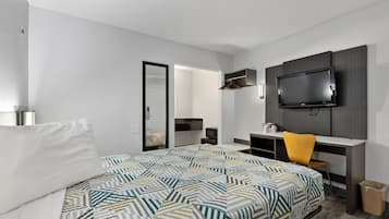 Una habitación de hotel con cama, escritorio, silla, televisor y espejo.