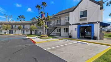 Un motel con un letrero de 'Welcome', un estacionamiento y un edificio con balcón.