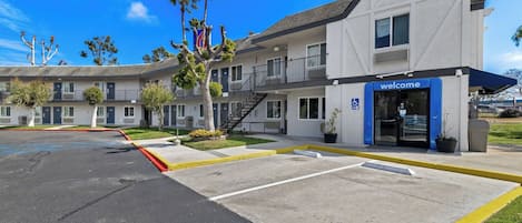 A motel with a 'Welcome' entrance, a parking lot, and a building with a balcony.