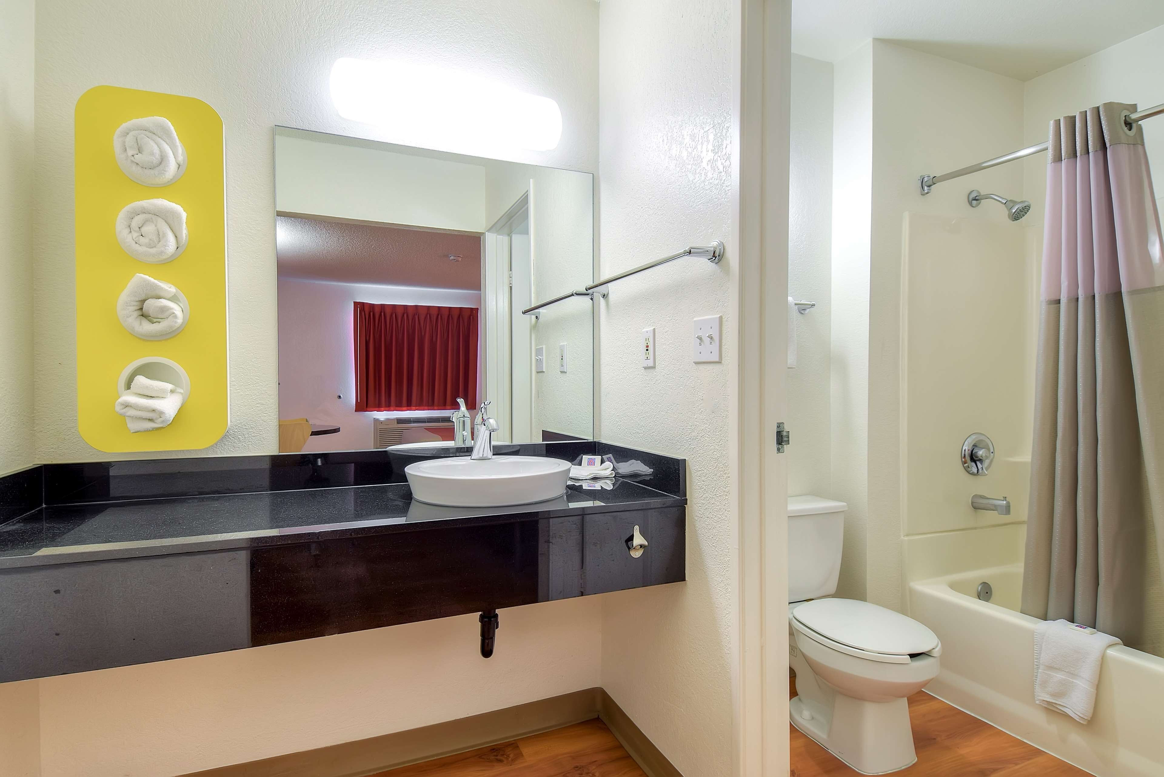 A bathroom with a black countertop, white sink, and a mirror above it. There is a shower area with a curtain and a bathtub.