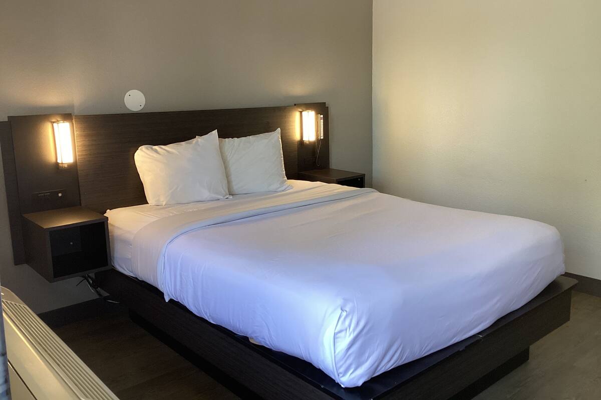 A neatly made bed with white linens, a dark headboard, and two bedside lamps on either side.
