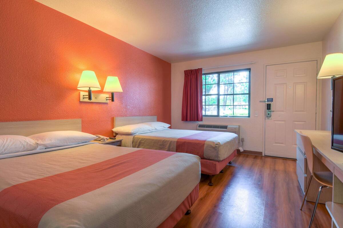 A hotel room with two beds, a desk, and a window with curtains.