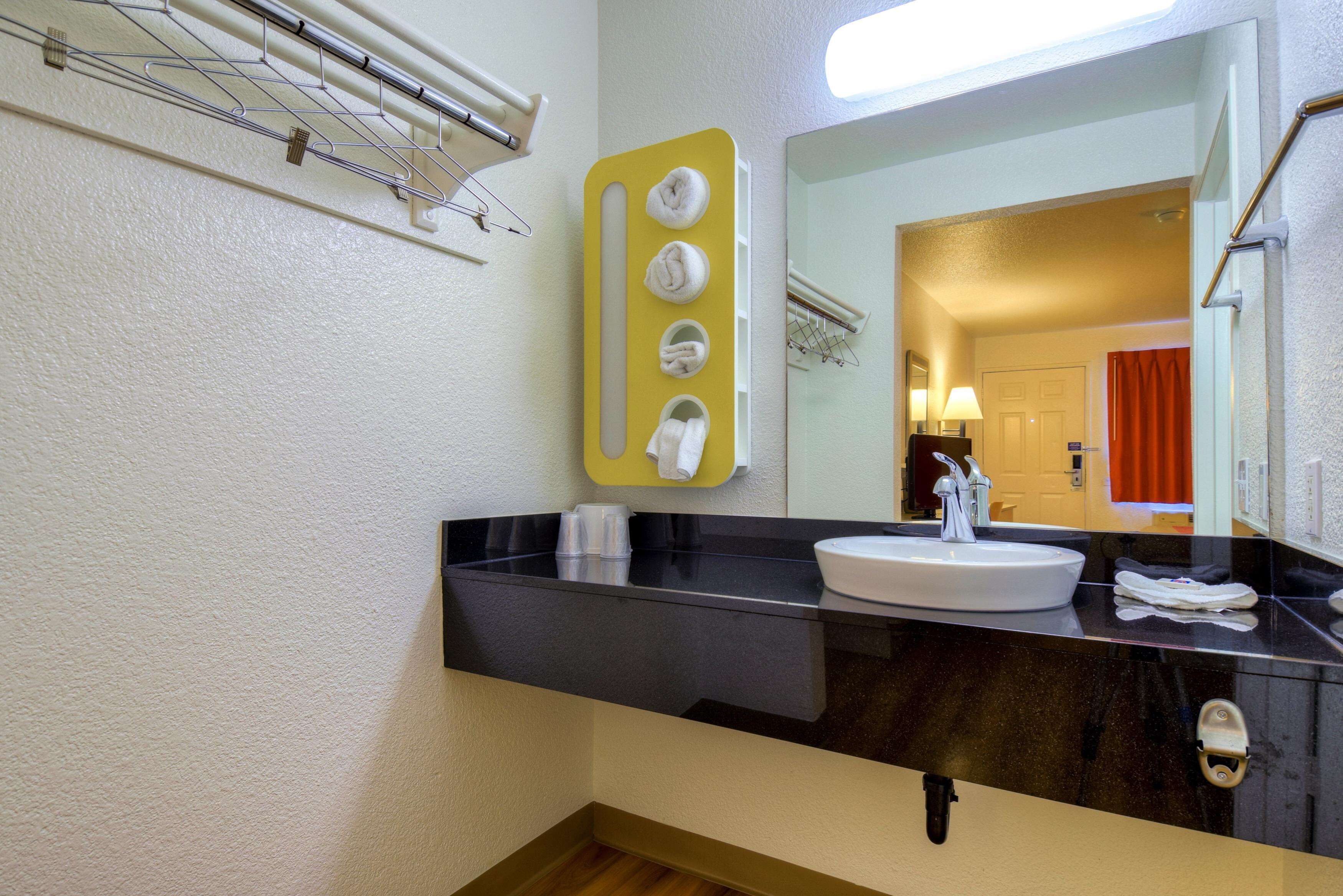 A bathroom with a black countertop, white sink, and a mirror. There are towels hanging on a rack above the sink.