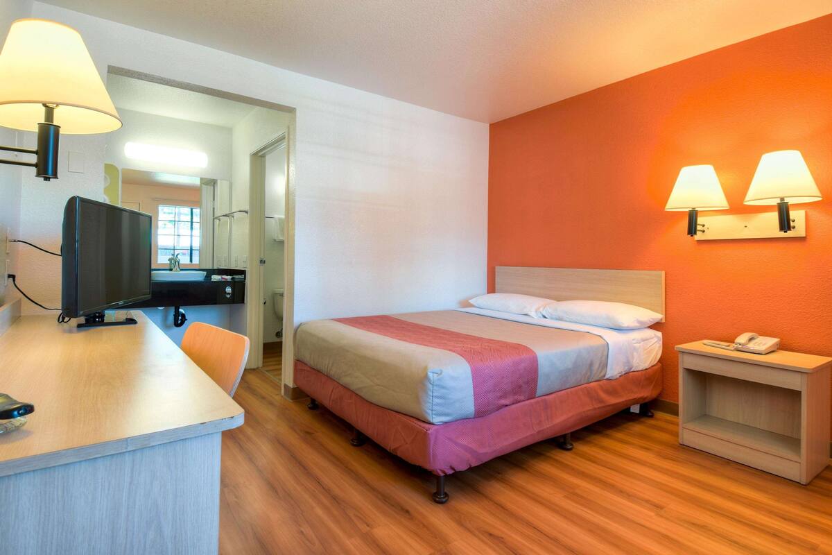 A hotel room with a bed, a desk with a television, and two wall-mounted lamps.