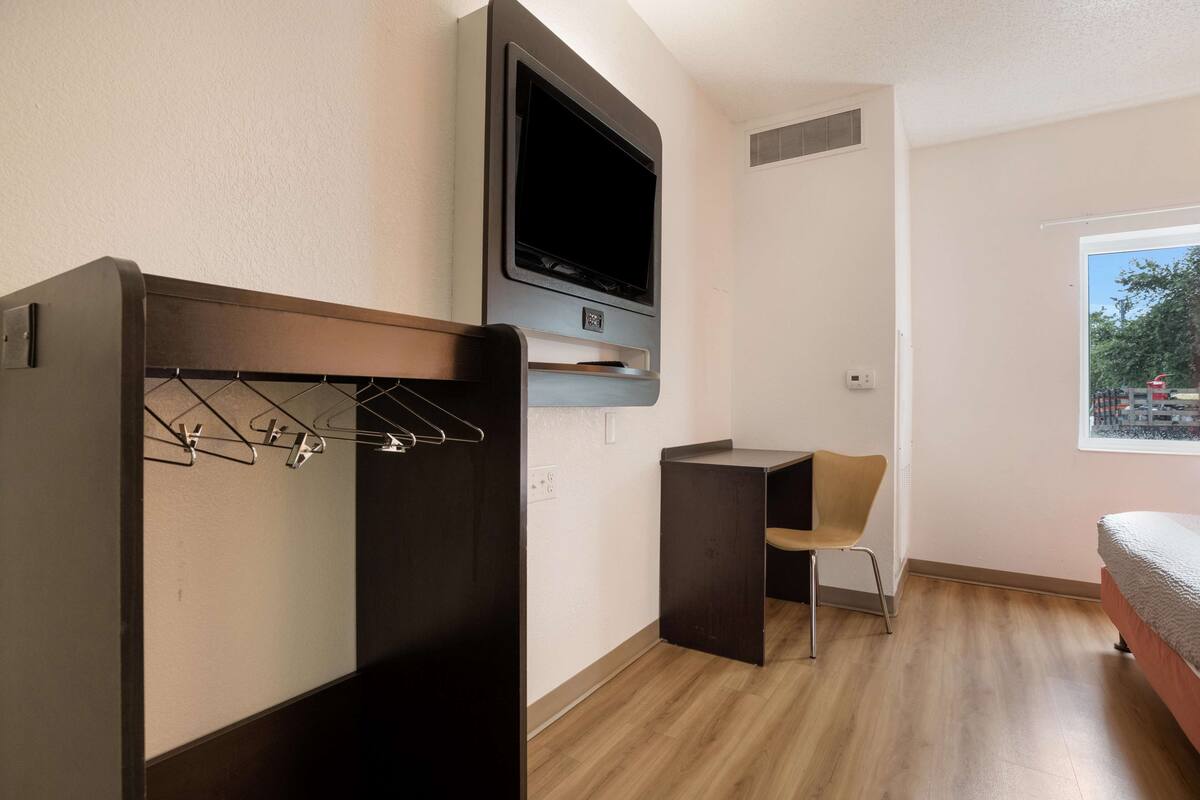 Ein kleines Zimmer mit Bett, Wand-Fernseher, Schreibtisch und Stuhl.