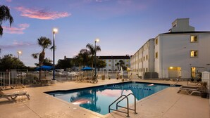 An outdoor swimming pool with lounge chairs and umbrellas, surrounded by a fence and palm trees. - Motel 6 Orlando, FL - International Dr (Orlando)
