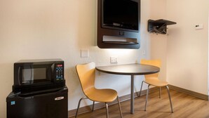 A compact room with a microwave, a small refrigerator, a TV mounted on the wall, and two chairs around a small table. - Motel 6 Orlando, FL - International Dr (Orlando)