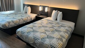 A hotel room with two beds, each with patterned bedding and headboards with wall-mounted lighting.