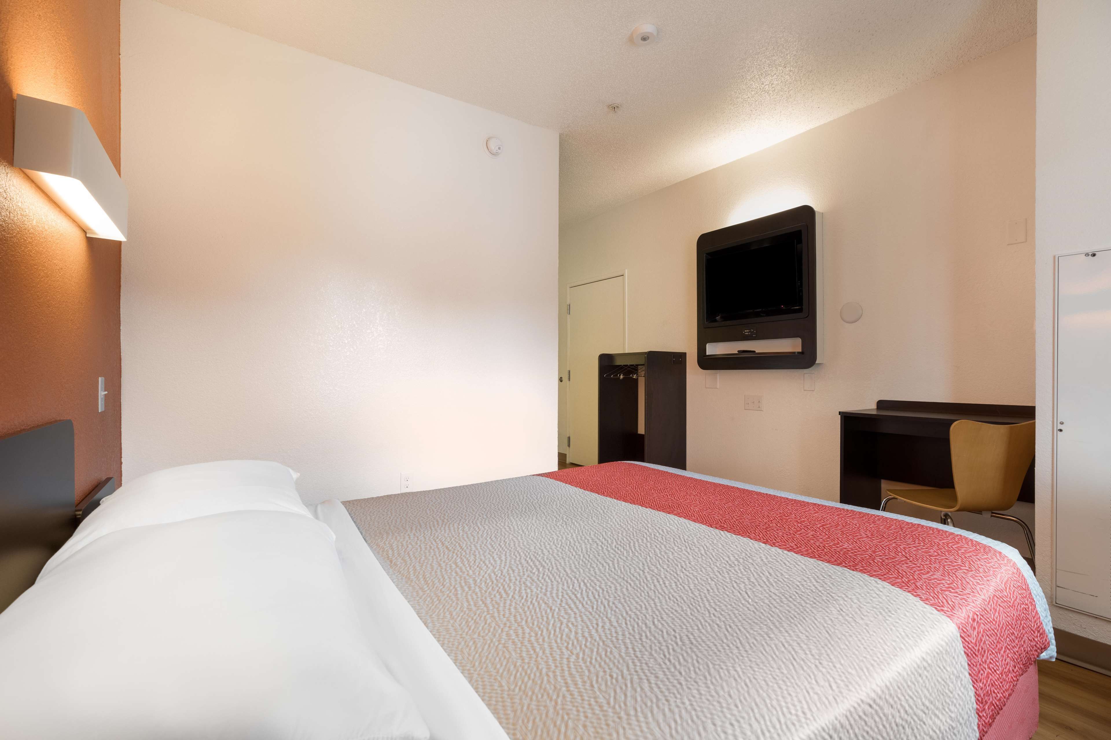 A hotel room with a bed, a desk, a chair, a television, and a door.