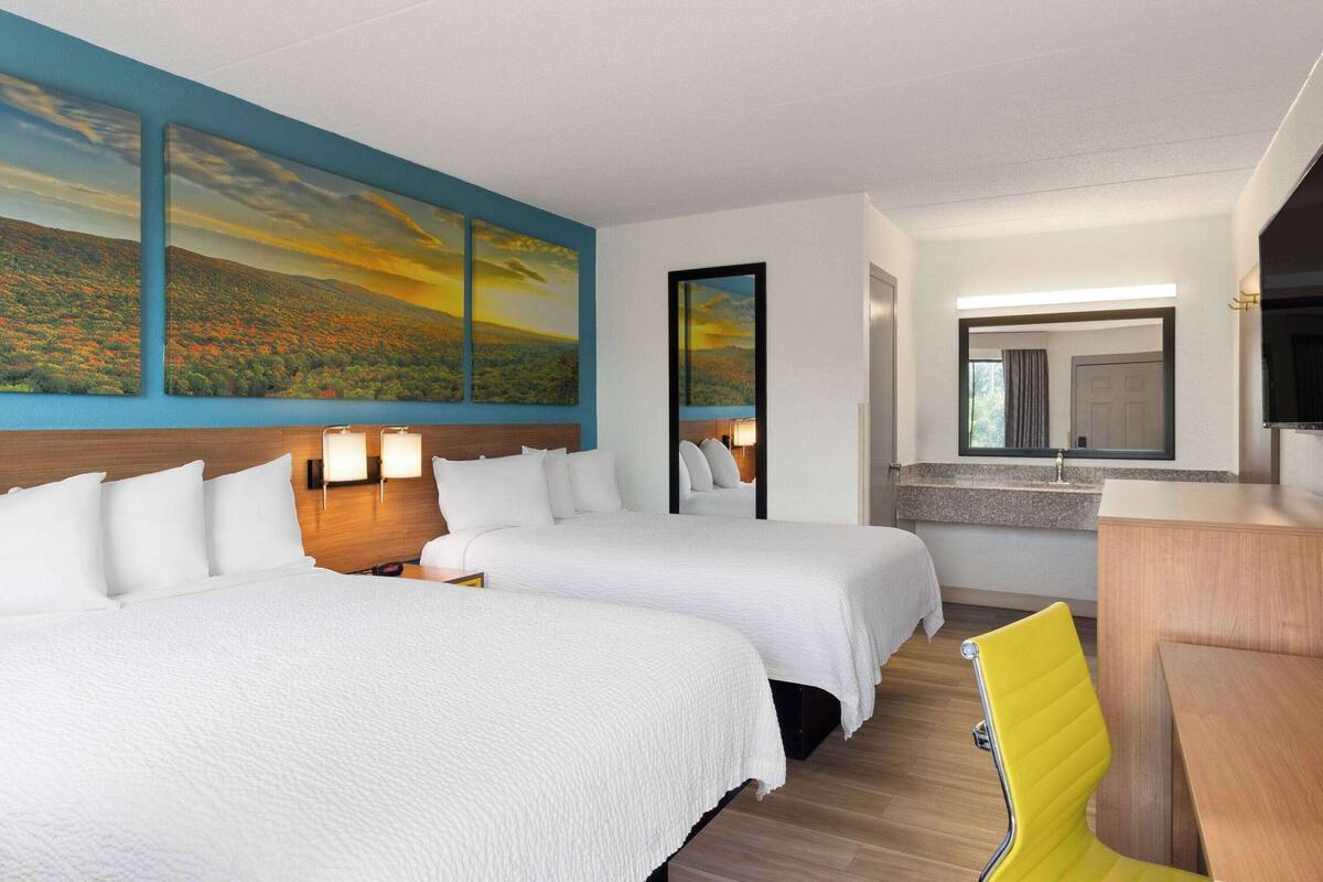 Habitación de hotel con dos camas, un escritorio, una silla, un espejo y un cuadro en la pared.