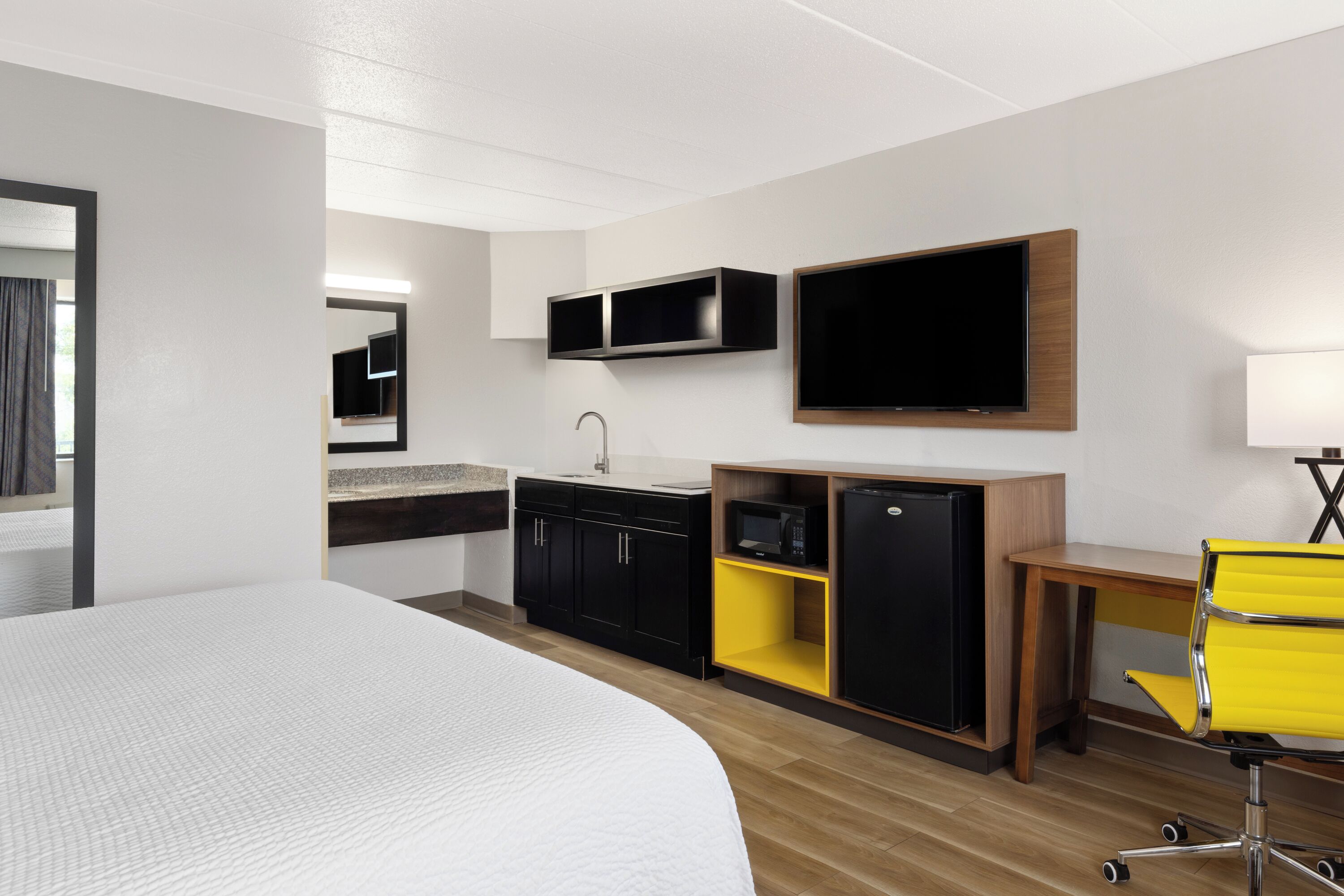 A hotel room with a large bed, a desk with a chair, a microwave, a refrigerator, a TV, and a sink.
