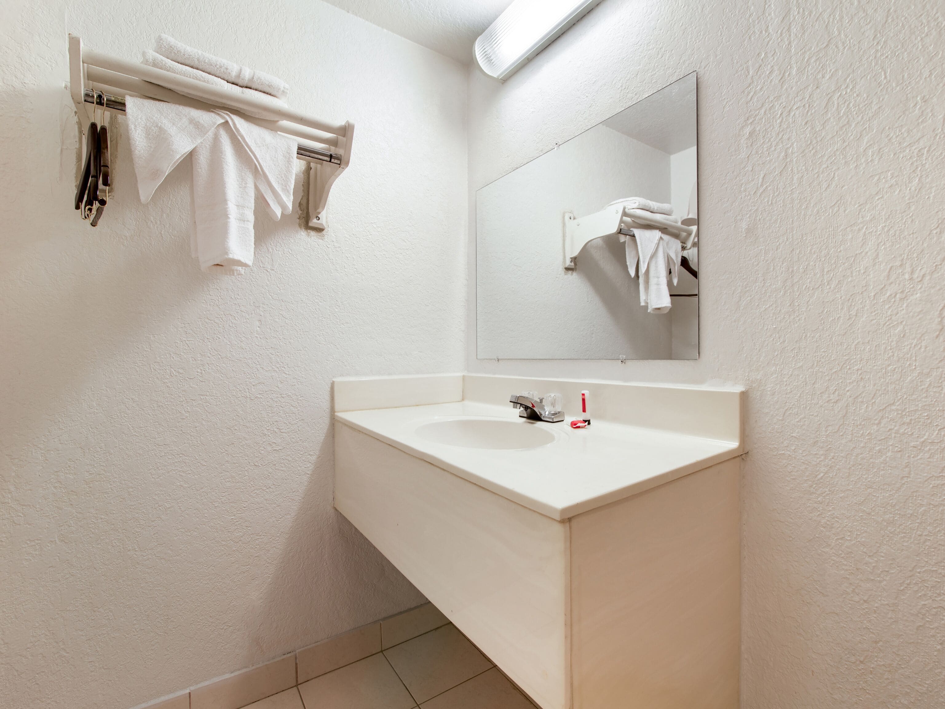 Une salle de bain avec un lavabo blanc, un miroir et un porte-serviettes avec des serviettes.