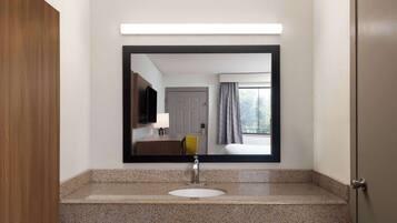 Un baño con encimera de granito, un lavabo blanco, un espejo grande y una puerta de madera.