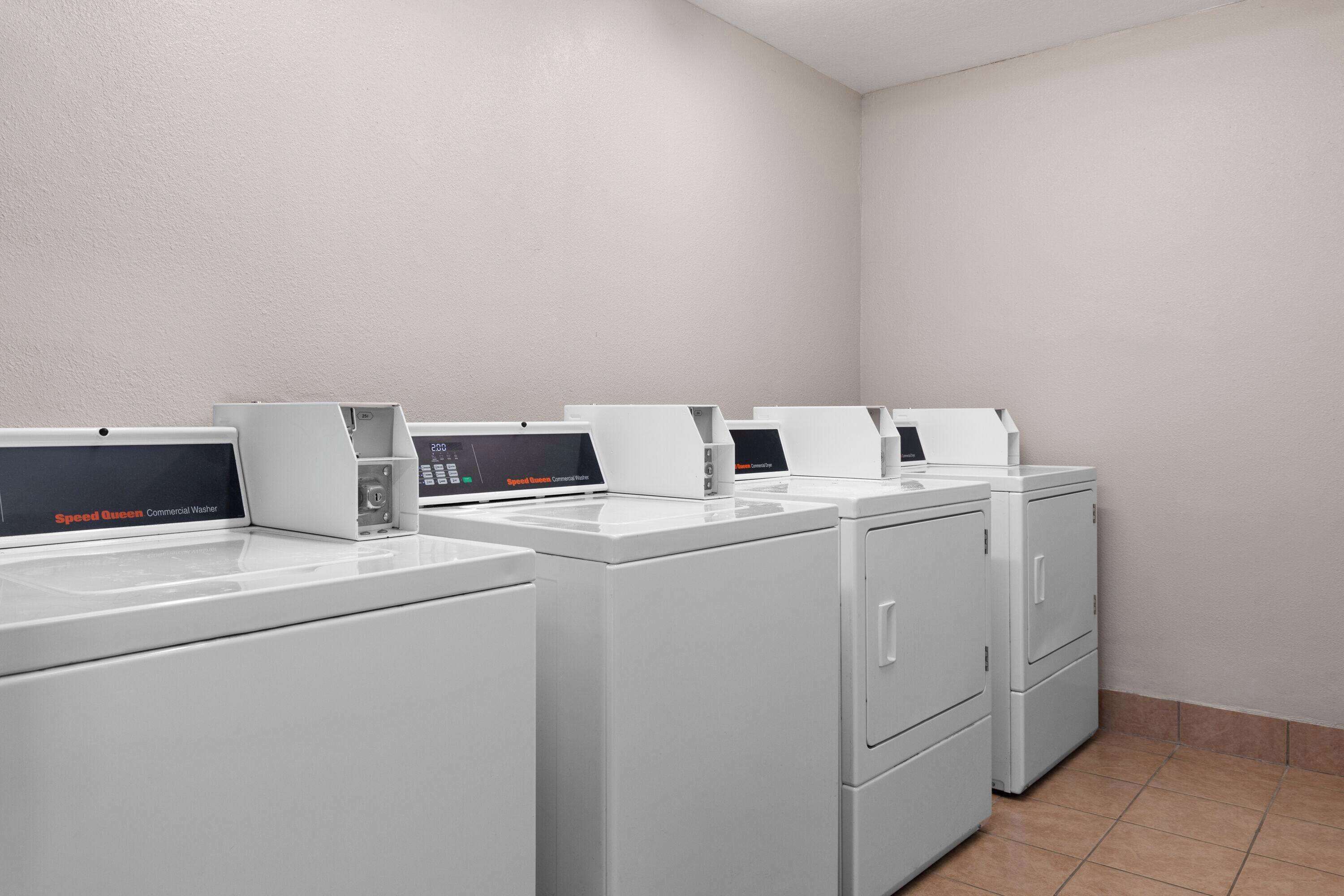 Une buanderie équipée de plusieurs lave-linge et sèche-linge blancs, d’un lave-linge professionnel de marque Speed Queen et d’un panneau de commande.